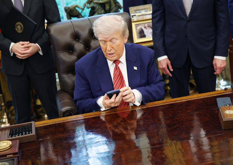 US President Donald Trump holds an Apple Inc. iPhone during an executive order signing in the Oval Office of the White House in Washington, DC, US, on Friday, May 23, 2025. Trump on Friday signed orders meant to accelerate the construction of nuclear power plants, including small, untested designs that offer the promise of rapid deployment but have yet to be built in the US.