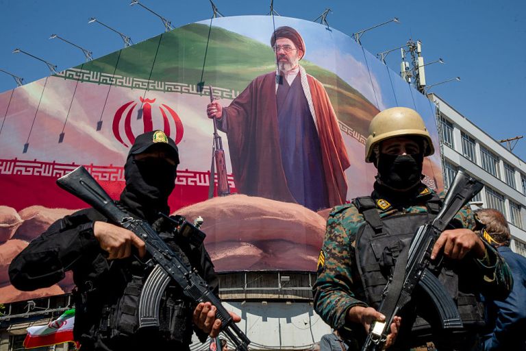 Members of the Iranian security forces stand guard under a large portrait of Iran's new Supreme Leader, Mojtaba Khamenei, during a memorial to mark the 40th day since his father, Ayatollah Ali Khamenei, was killed in US-Israeli joint strikes, on April 9, 2026 in Tehran.
