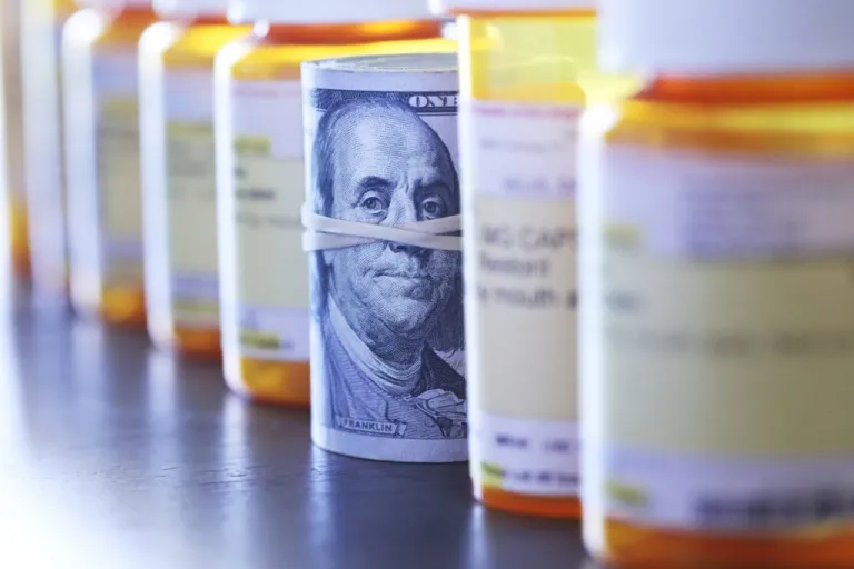 A roll of one hundred dollar bills in line with pill bottles.