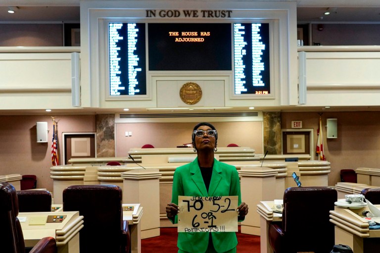 Alabama state Rep. Juandalynn Givan stands with a sign in a green jacket