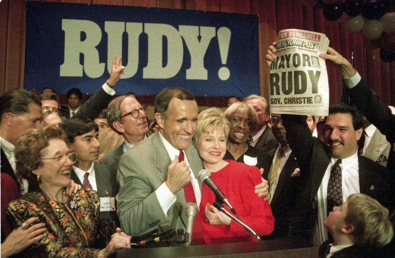 New York Mayor-elect Rudolph Giuliani hugs his wife Donna as a supporter holds a newspaper with a headline declaring Giuliani the city's new mayor