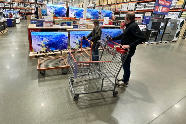 Shoppers stop their carts to observe big-screen televisions on display in a Costco warehouse.