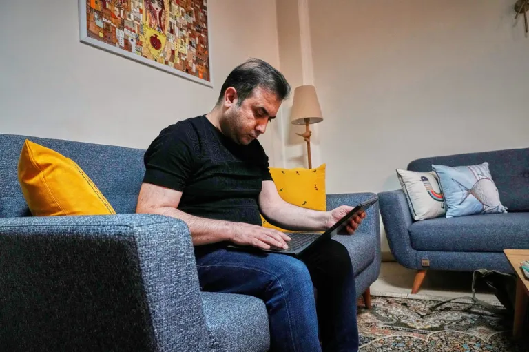 Mehdi Alishir looks at his laptop in his living room in Tehran, Iran.