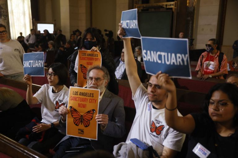People in the audience hold up signs in support of immigrants as the Los Angeles City Council considers a 