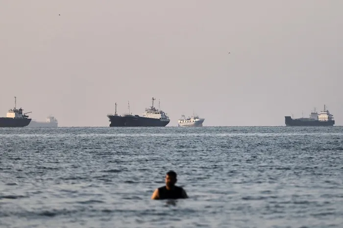 A person stands on shallow water as cargo and commercial vessels are anchored in the Strait of Hormuz.