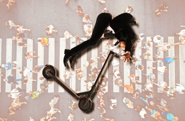 A topdown view of a pedestrian's silhouette lays on the ground next to their fallen scooter transportation as their hand extends up to the sky as if for help.