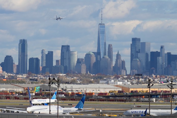 The New York City skyline is seen behind a plane approaching Newark International Airport.
