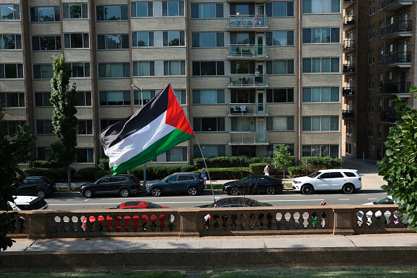 WASHINGTON, DC - JULY 02: A protester carries a Palestinian flag near Meridian Hill Park before an event with members of the U.S National Guard and U.S. Secretary of War Pete Hegseth on July 02, 2026 in Washington, DC. Hegseth and other members of U.S. President Donald Trump's administration visited the park to speak to guard members and to tout the DC Safe And Beautiful Task Force.
